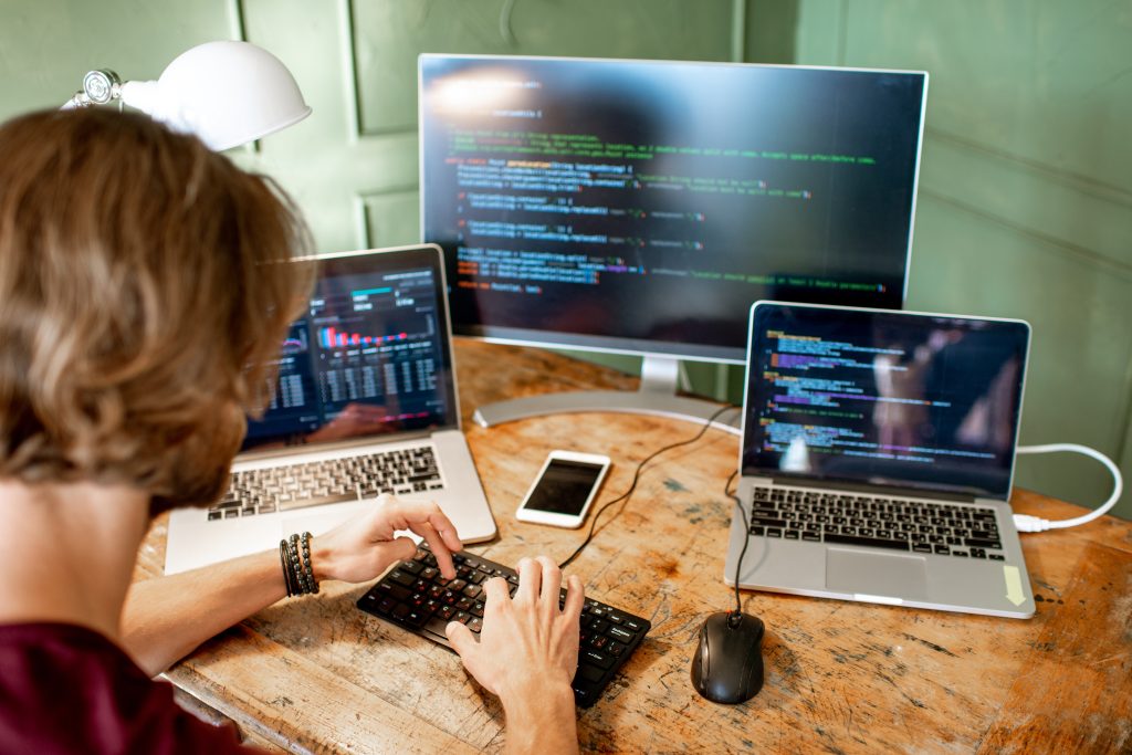 Programmer creating a mobile app at three computer screens